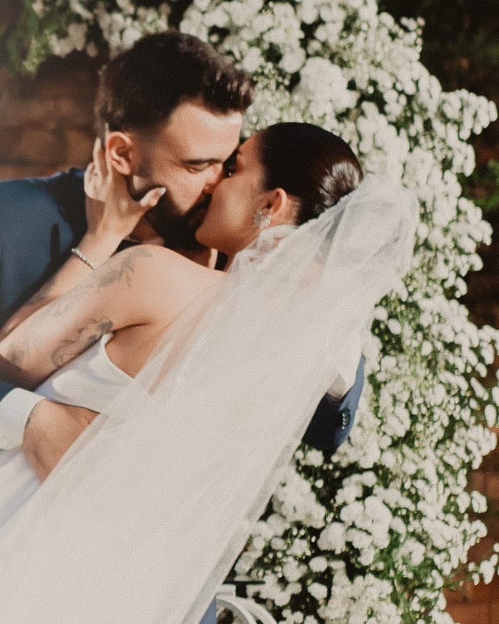 Noivos se beijando em frente a uma parede de flores brancas